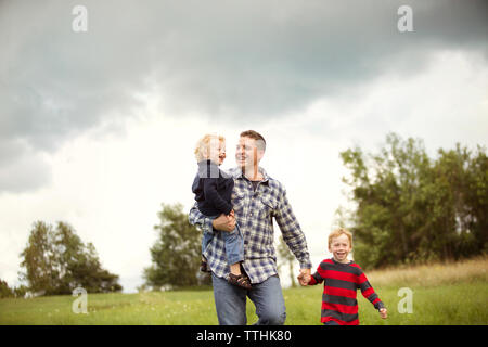 Père souriant avec fils on grassy field against sky Banque D'Images