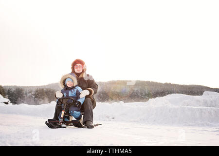 Portrait of happy mother sur un traîneau en hiver contre le ciel clair Banque D'Images