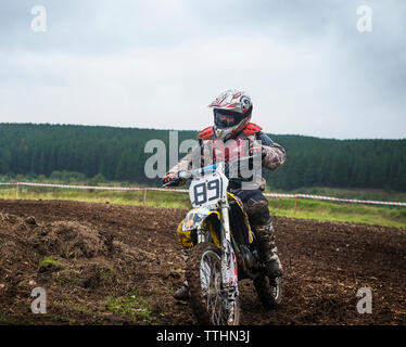 Biker riding dirt bike sur terrain against sky Banque D'Images