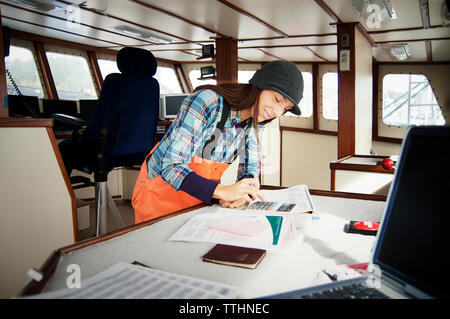 Femme à l'aide de la Calculatrice et écrire des documents en bateau de pêche Banque D'Images
