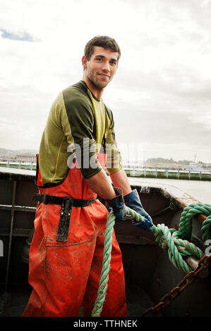 Portrait of smiling pêcheur tirant sur la corde de bateau de pêche des sky Banque D'Images