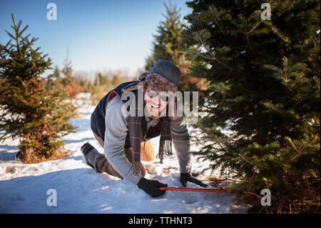 Homme heureux coupant l'arbre de noël sur le champ couvert de neige Banque D'Images