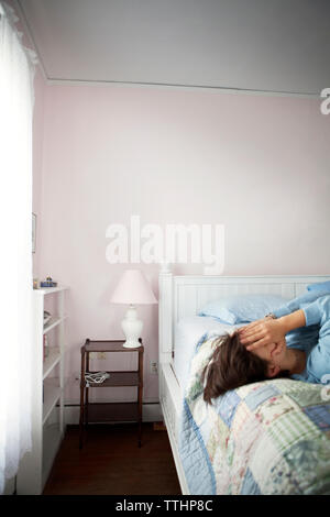 Femme couvrant le visage avec les mains si lying on bed Banque D'Images