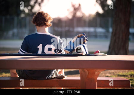 Vue arrière du roller hockey player sitting on park bench Banque D'Images