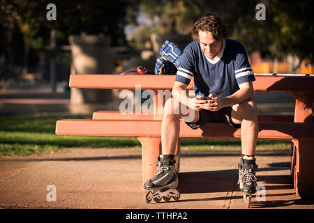 Roller hockey player using mobile phone while sitting on park bench Banque D'Images