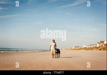 Man Walking with dog on shore against sky Banque D'Images