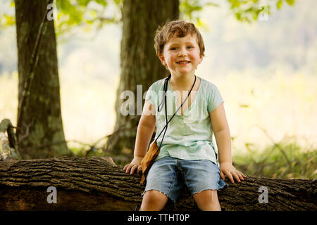 Portrait of cute boy sitting on fallen tree trunk Banque D'Images