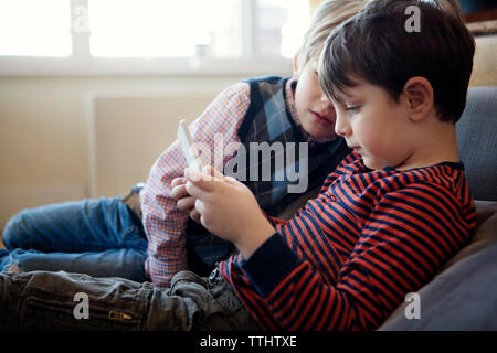Siblings playing video game while sitting on sofa at home Banque D'Images