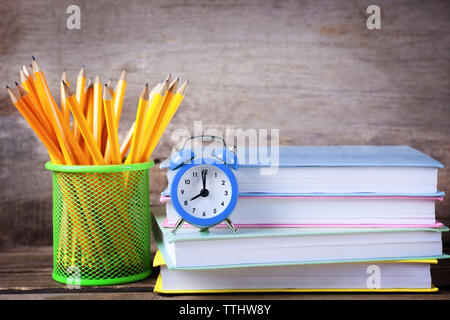 Ensemble de crayons en support de métal, pile de livres et réveil sur fond de bois Banque D'Images