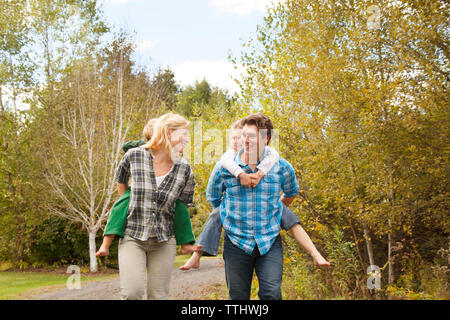 Les parents qui piggyback ride aux enfants contre des arbres Banque D'Images