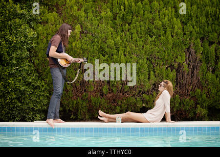 Homme jouant de la mandoline et woman sitting by swimming pool Banque D'Images