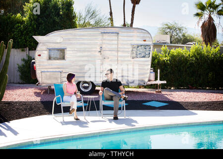 Couple sitting on chair par piscine contre camping-van Banque D'Images