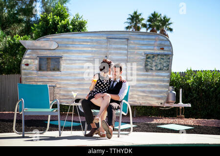 Cheerful couple sitting on chair contre camping-van Banque D'Images