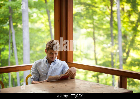 Boy reading book while sitting on chair par table Banque D'Images