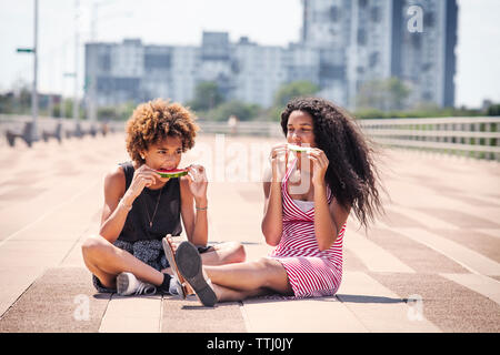 Female friends eating watermelon while sitting on pier Banque D'Images