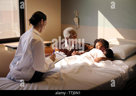 Rapport écrit du médecin tandis que grand-père regardant girl in hospital Banque D'Images