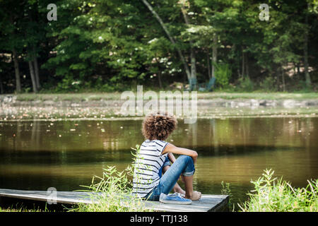 Vue arrière du teenage girl sitting on jetty at Lake Banque D'Images