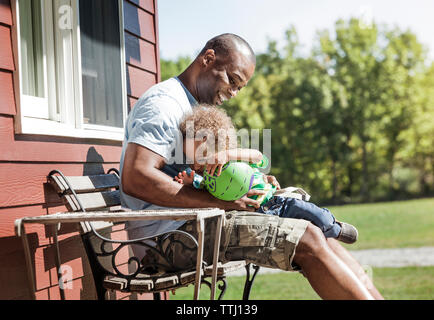 Heureux père et fils assis avec balle sur banc arrière-cour Banque D'Images