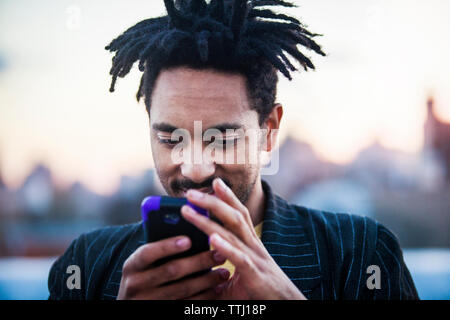 Smiling man using mobile phone against sky Banque D'Images