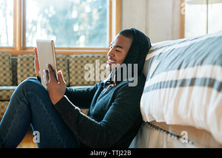 Happy man using tablet computer while sitting par bed at home Banque D'Images