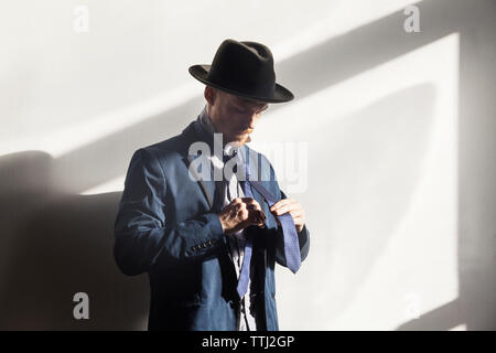 Man adjusting necktie debout contre le mur à la maison blanche Banque D'Images