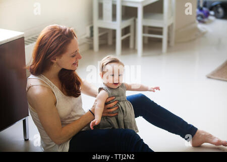 Mother holding daughter while sitting on floor at home Banque D'Images