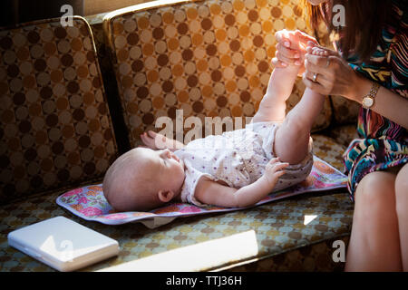 Portrait of woman holding baby girl's feet on sofa Banque D'Images