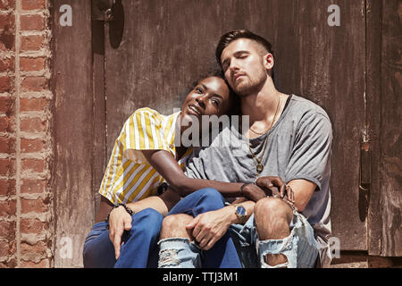 Multi-ethnic couple relaxing contre la porte en bois Banque D'Images