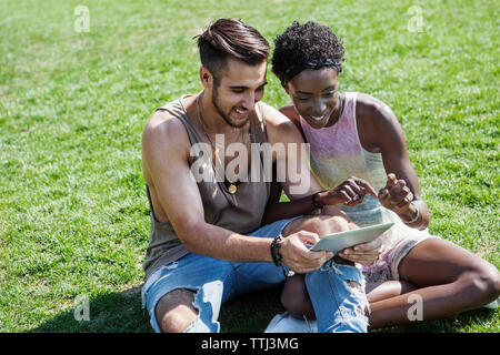 Smiling couple using tablet computer while sitting on grassy field Banque D'Images