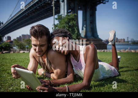 Heureux couple using tablet computer couchée sur terrain avec pont de Manhattan en arrière-plan Banque D'Images