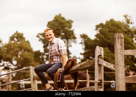 Portrait d'éleveur assis sur main courante contre le ciel Banque D'Images