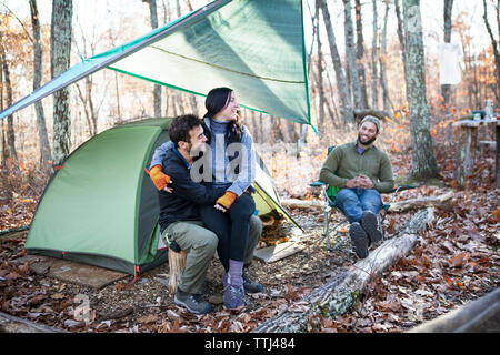 Ami(e) à la recherche de couple tout en restant assis sur les souches d'arbre par tente en forêt Banque D'Images