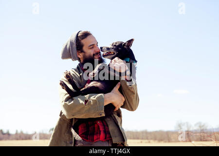 Happy man carrying dog debout contre le ciel clair Banque D'Images