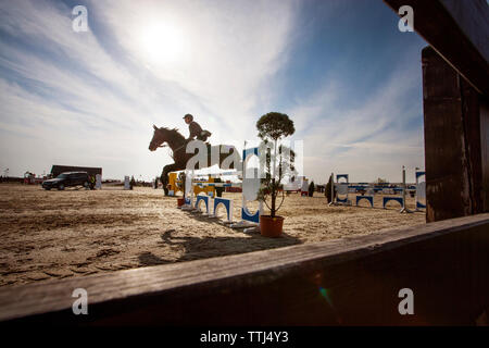 Vue de côté de l'homme cheval d'équitation sur obstacle contre sky Banque D'Images
