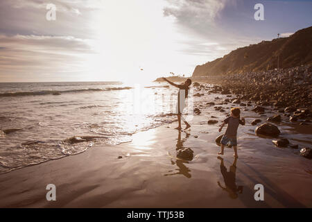 Père et fils jetant des pierres en mer pendant le coucher du soleil Banque D'Images