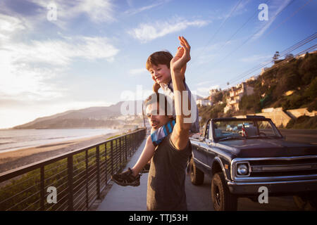 Portrait of father carrying son on shoulders pendant le coucher du soleil Banque D'Images