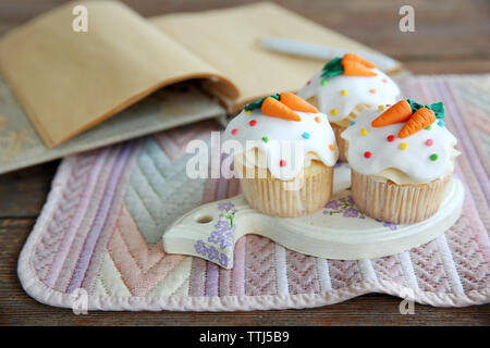 Cupcakes avec glaçage décoratif et carottes sur support en bois Banque D'Images