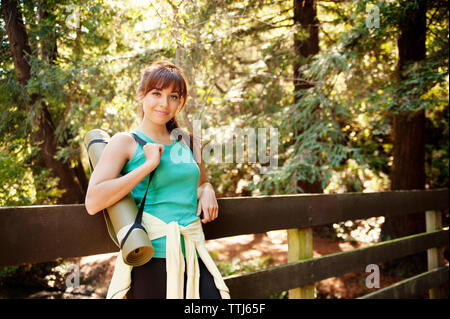 Portrait of woman carrying tapis d'exercice en position debout by railing in forest Banque D'Images