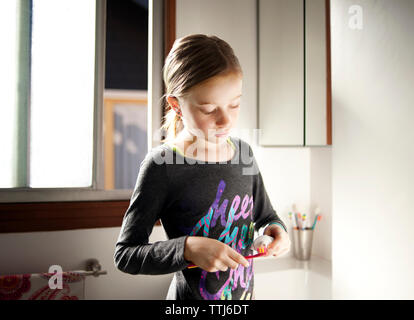 Girl putting dentifrice sur une brosse à dents dans la salle de bains Banque D'Images