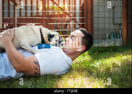 L'homme jouant avec le pug on grassy field in backyard Banque D'Images