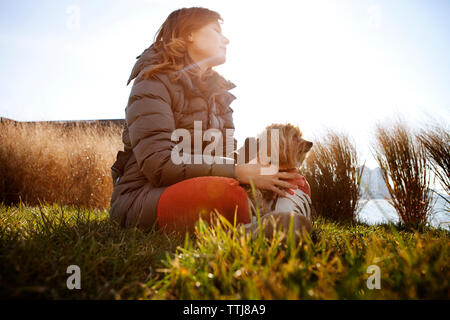 Low angle view of woman with dog sitting sur terrain contre ciel clair Banque D'Images