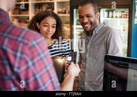 Couple heureux à la propriétaire à glisser une carte de crédit en magasin Banque D'Images