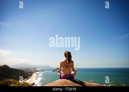 Woman meditating while sitting on rock par mer Banque D'Images