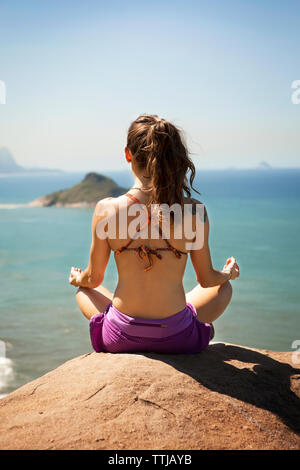 Rear view of woman meditating while sitting on rock Banque D'Images