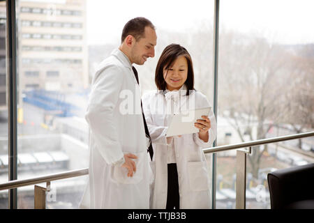 Happy doctor showing tablet computer à collègue debout contre l'hôpital dans la fenêtre Banque D'Images