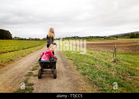 Girl pulling soeur assis dans un chariot sur le chemin de terre Banque D'Images