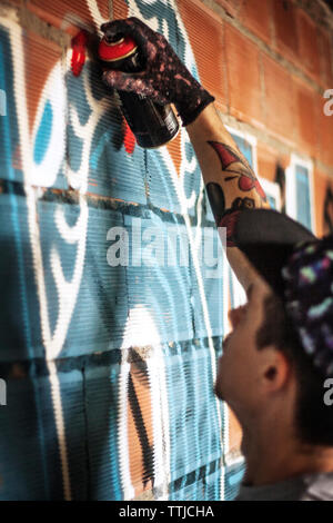 Man spraying graffiti sur mur de brique Banque D'Images