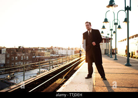 homme d'affaires attendant le train à la station de métro contre ciel dégagé Banque D'Images