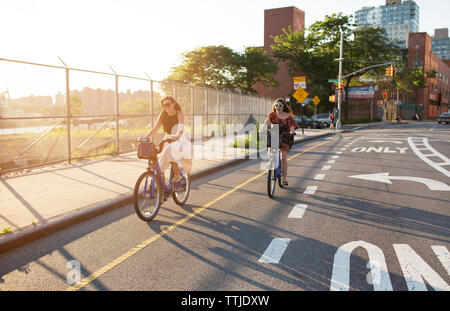 Happy female friends riding bicycle on city street Banque D'Images