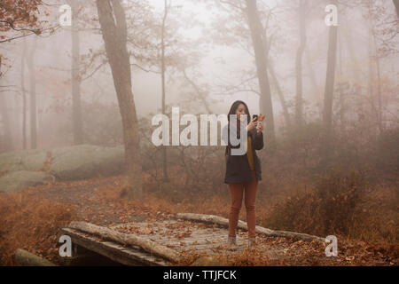 Photographier une femme par le biais de smart phone en étant debout sur la passerelle en forêt Banque D'Images
